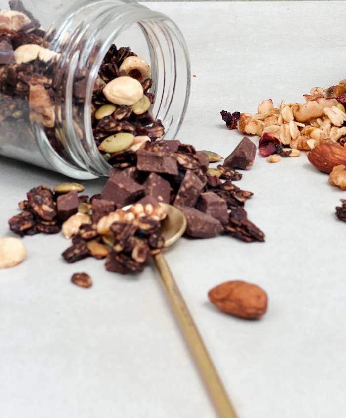 Close-up of a spilled jar of homemade granola mix with chocolate and nuts.